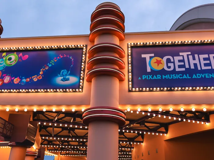 Auvent illuminé d’ampoules avec deux affiches, personnages Pixar et titre TOGETHER, entrée du spectacle au Parc Disney Adventure World au crépuscule.