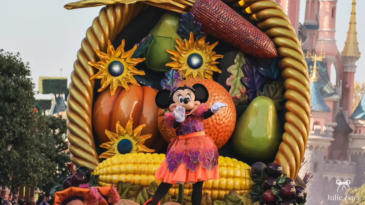 Minnie Mouse en costume d’automne orange et violet devant une corne d’abondance géante garnie de citrouilles et de tournesols, pendant la saison d’Halloween à Disneyland Paris.