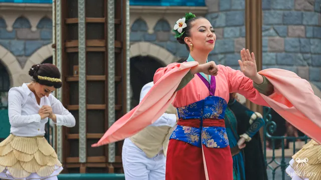 La princesse Mulan, tenue rose et rouge avec une fleur dans les cheveux, danse devant le château à Disneyland Paris.