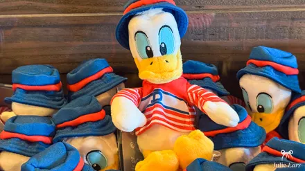 Peluches d’épaule de Donald en tenue parisienne, béret bleu et marinière rayée, empilées dans une boutique de Disneyland Paris.