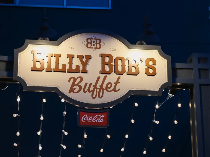 Enseigne éclairée « Billy Bob’s Buffet » avec guirlandes lumineuses et logo Coca-Cola à la tombée de la nuit.