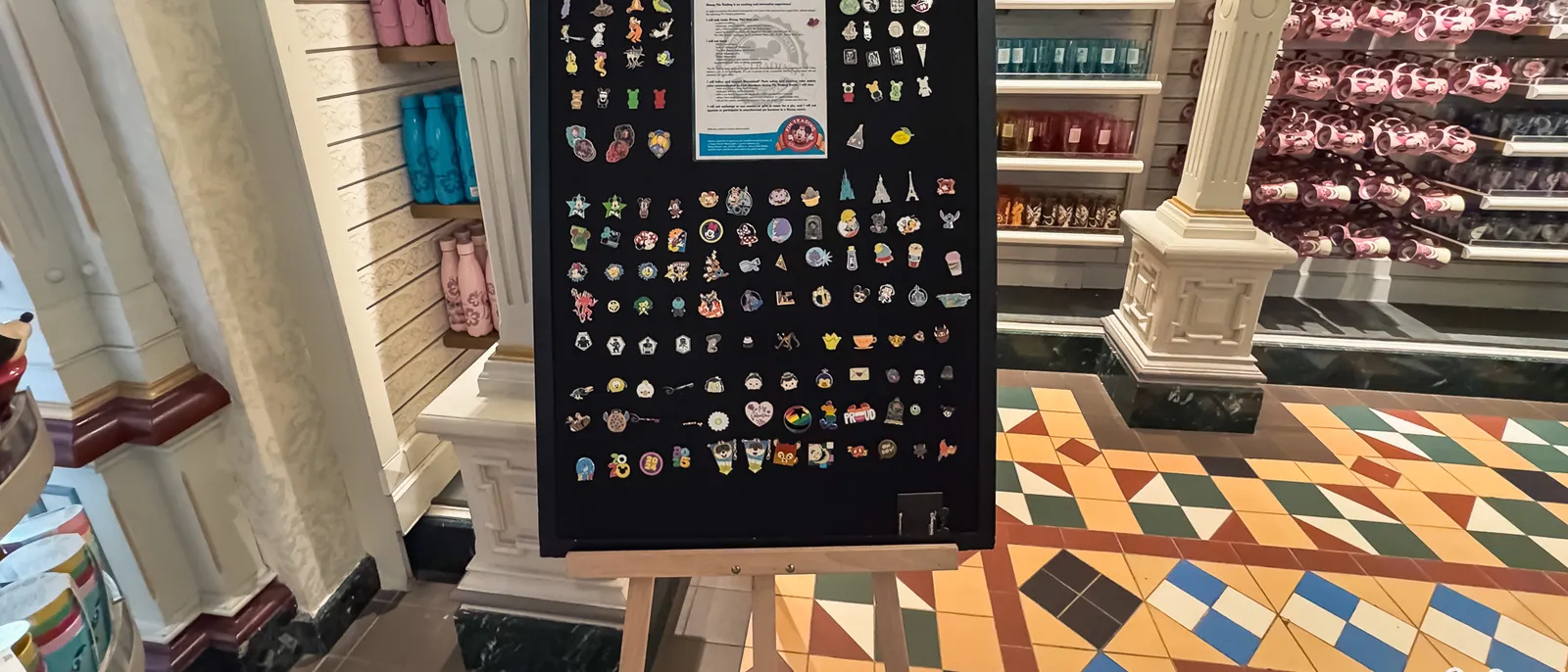 Grand tableau noir couvert de pin’s Disney sur un chevalet, dans une boutique de Disneyland Paris.