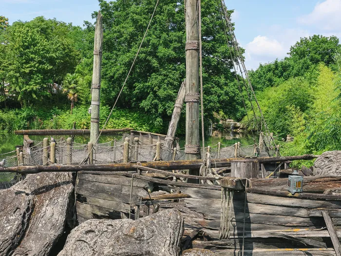 Bateau pirate en bois amarré parmi les rochers au bord de l’eau, entouré de verdure à Adventure Isle