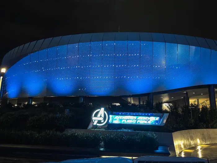 Façade arrondie d’Avengers Assemble: Flight Force éclairée en bleu la nuit, enseigne allumée au Marvel Avengers Campus.
