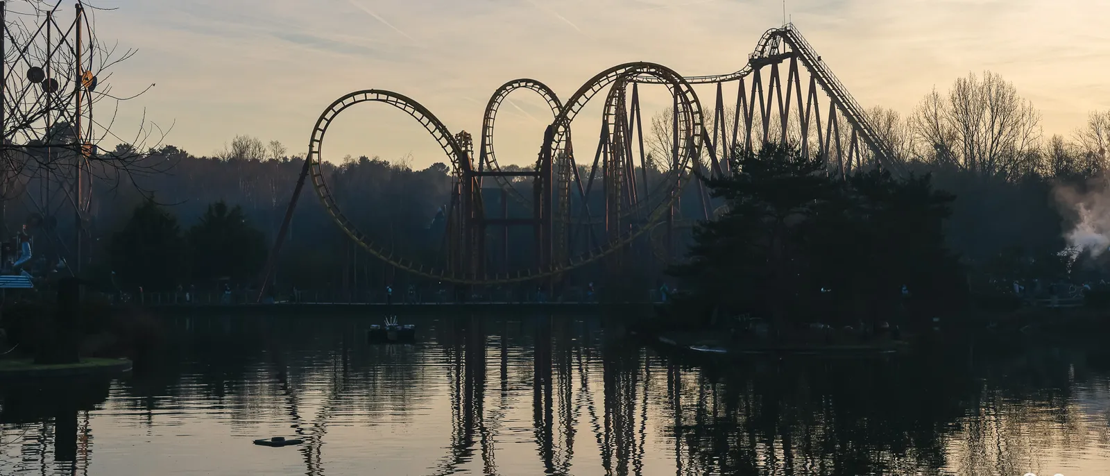 Loopings de Goudurix en silhouette au coucher du soleil, reflétés dans le lac bordé d’arbres nus