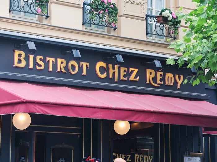 Enseigne dorée Bistrot Chez Rémy au-dessus d’un store bordeaux et de fenêtres fleuries, restaurant Ratatouille