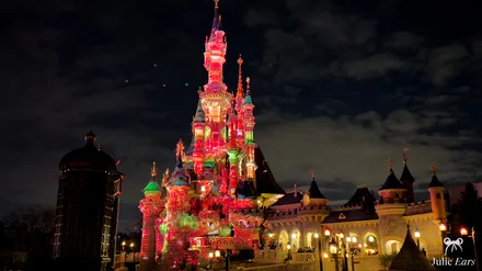 Le château de la Belle au Bois Dormant illuminé de projections de Noël rouges et vertes la nuit à Disneyland Paris
