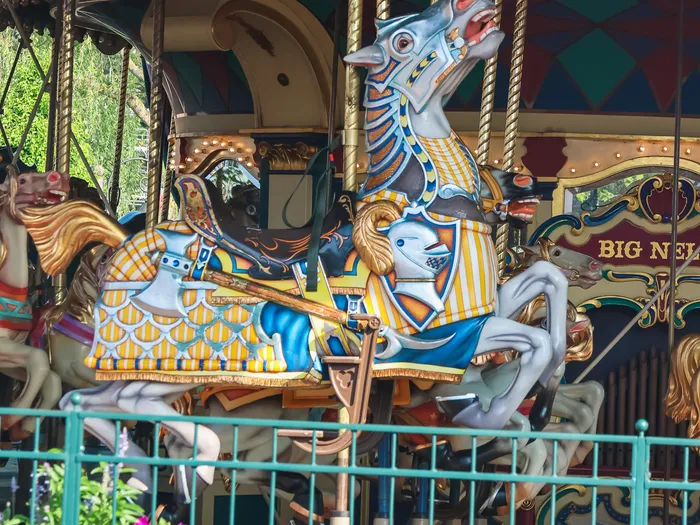 Cheval de manège peint en bleu, blanc et or du Carrousel de Lancelot, cabré au-dessus des massifs fleuris.