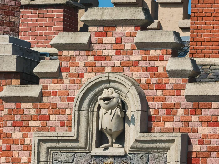Façade crénelée en brique de Toad Hall Restaurant, crapaud sculpté et parasol vert en contrebas