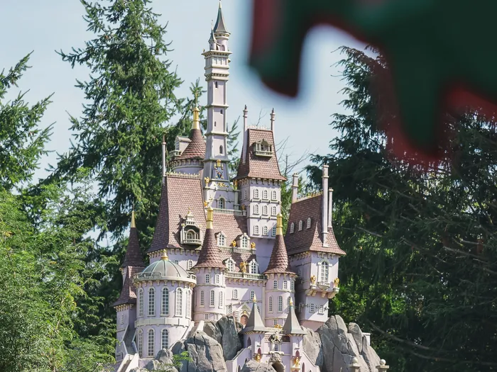 Château miniature rose et gris entouré de sapins, décor traversé par le petit train Casey Jr à Fantasyland