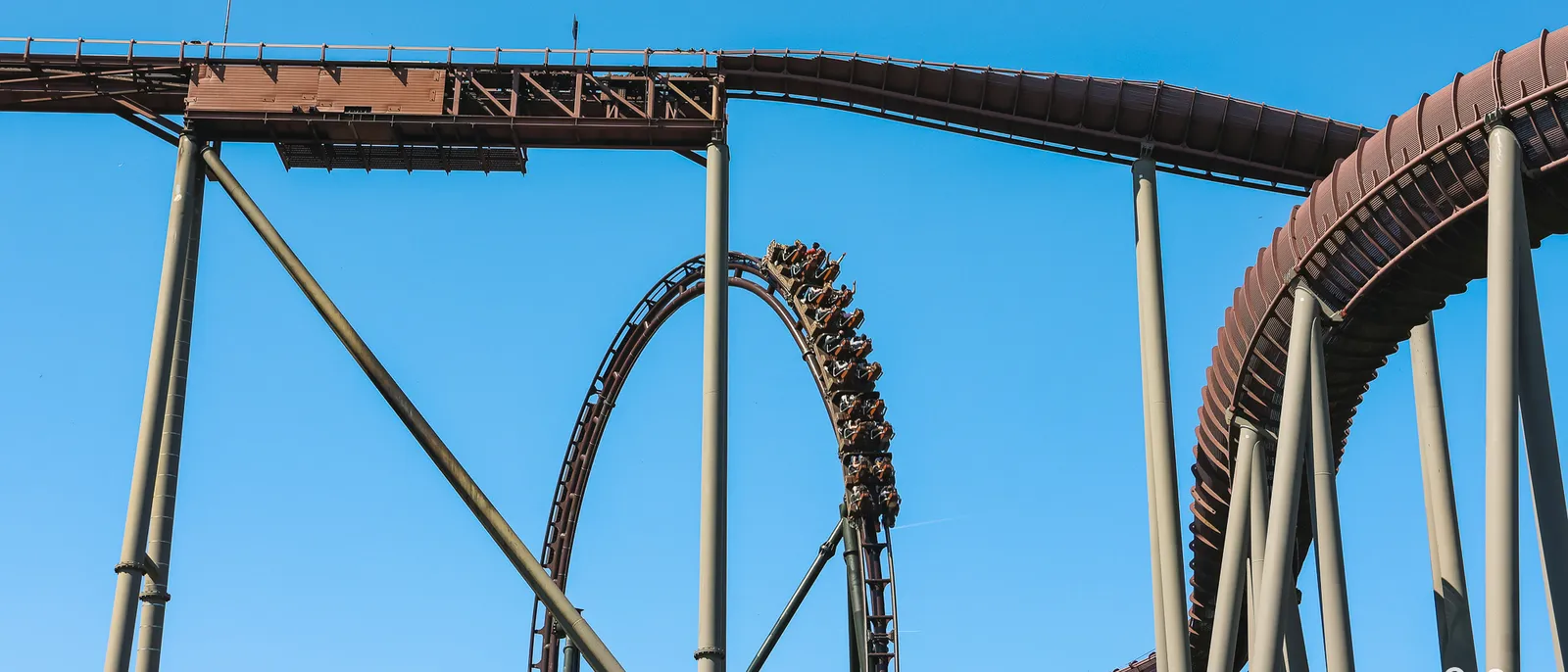 Train de Toutatis en pleine inversion sur la voie brune du coaster, piliers d’acier sur fond de ciel bleu sans nuage