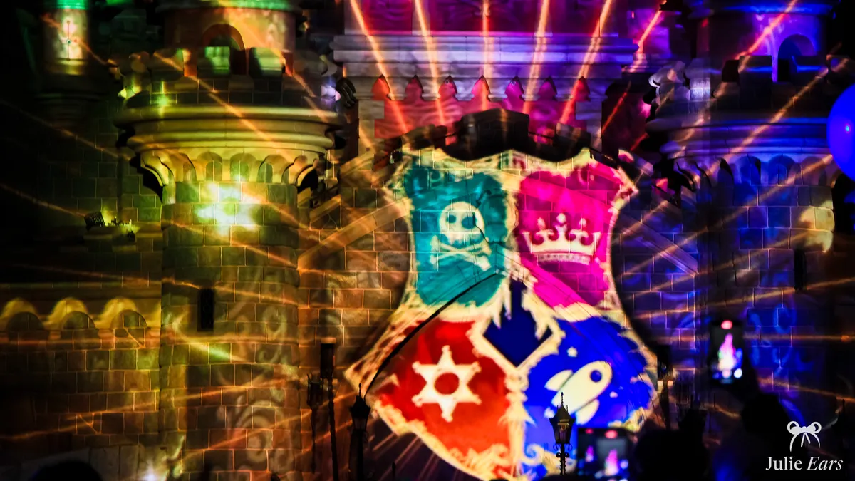 Coat of arms with land symbols (pirate skull, crown, sheriff’s star, rocket) projected onto Sleeping Beauty Castle at Treasure Night 2024