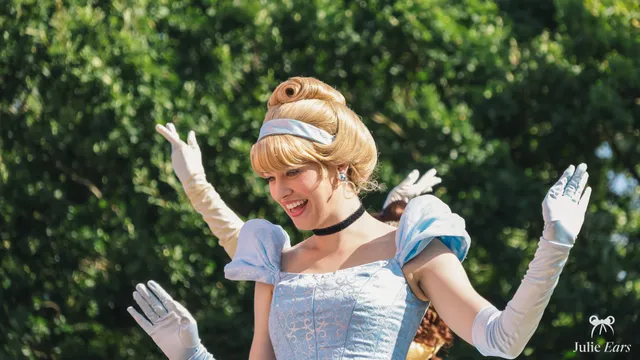 La princesse Cendrillon, chignon blond et robe bleu clair avec de longs gants blancs, lève les bras en souriant lors de la parade à Disneyland Paris.