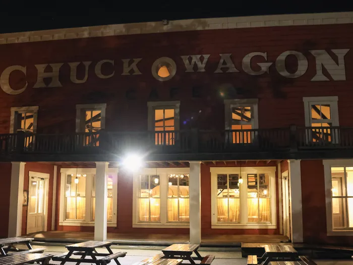 Façade en bois rouge du Chuck Wagon Café éclairée la nuit, avec tables de pique-nique en terrasse