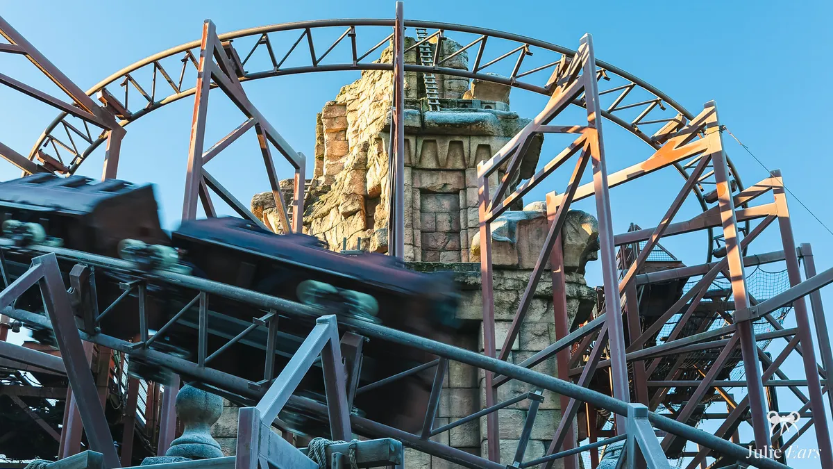 Mine train racing at full speed, motion blurred, on the Indiana Jones and the Temple of Peril track in front of the ruined Adventureland temple