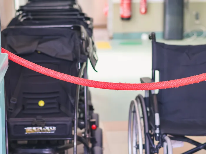 Red rope stretched in front of a row of black pushchairs, with a wheelchair on the right, its handle held by a hand, at Disneyland Paris.