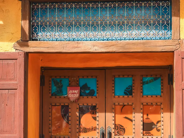 Closed studded wooden door of the Les Trésors de Schéhérazade shop at Disneyland Paris, with a bilingual "Closed" sign and stained glass