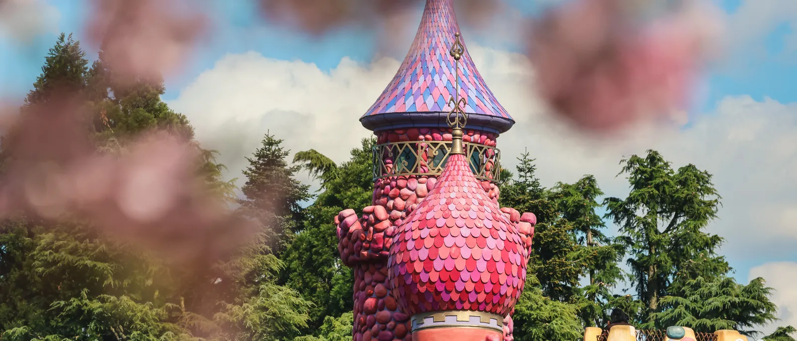 Tourelle rose aux tuiles arrondies du château de la Reine de Cœur, arbres verts et ciel nuageux à Fantasyland.