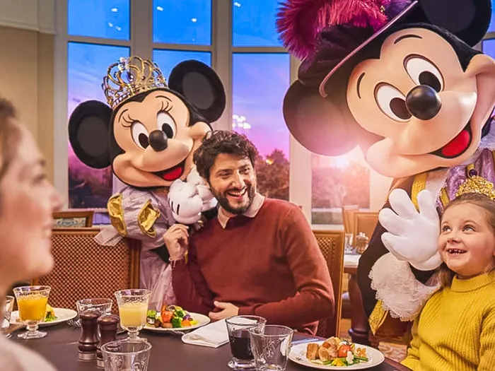 Mickey et Minnie en habits royaux saluent une famille attablée au restaurant Royal Banquet du Disneyland Hotel.