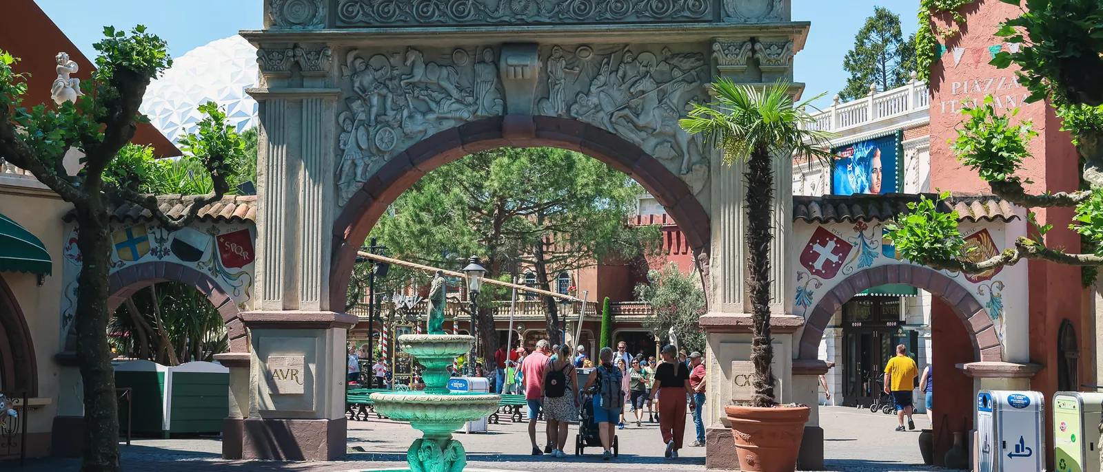 Arche de pierre sculptée et fontaine verte au fil d’une allée pavée à Europa-Park