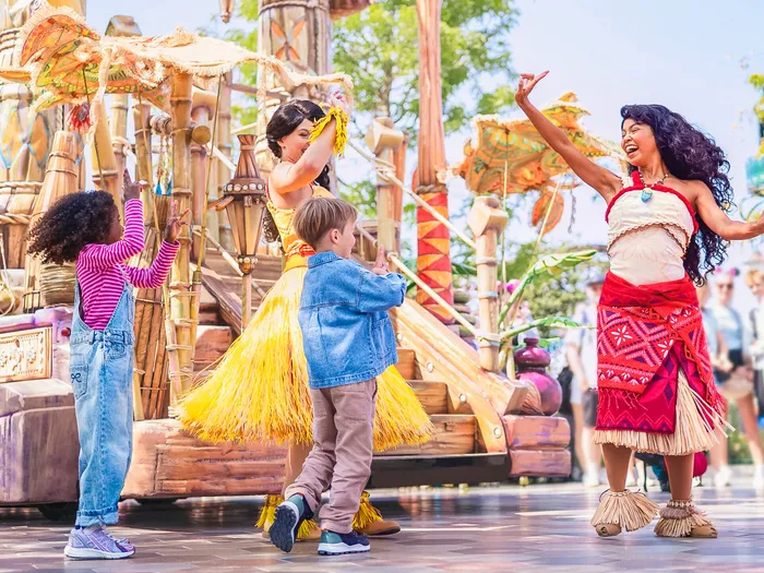 Vaiana dansant avec des enfants en jupes de paille devant un char tropical