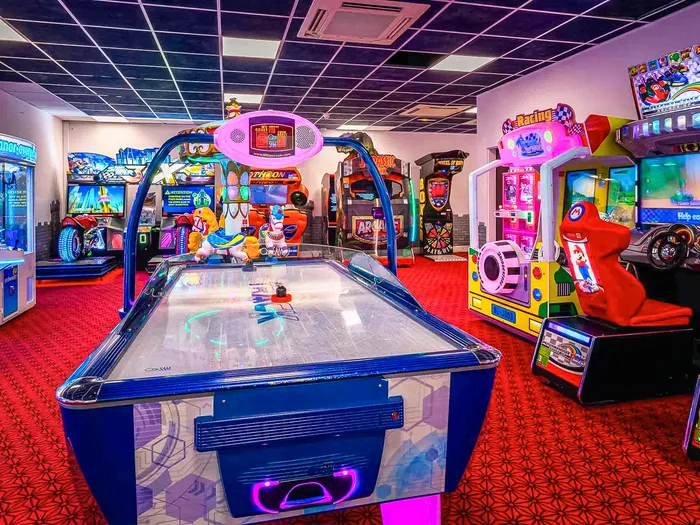 Salle d’arcade de l’Explorers Hotel avec air hockey et bornes de jeux lumineuses.