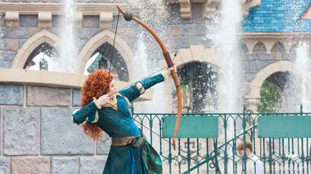 Merida from Brave drawing her bow in front of the castle during World Princess Week at Disneyland Paris