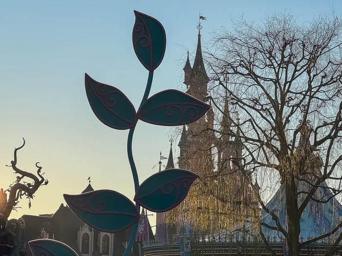 Grande fleur décorative de Fantasyland en contre-jour, les tours du Château derrière au lever du soleil.