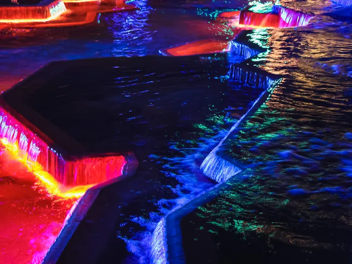 Cascades et bassins de Discoveryland éclairés en rouge, bleu et vert dans la nuit.