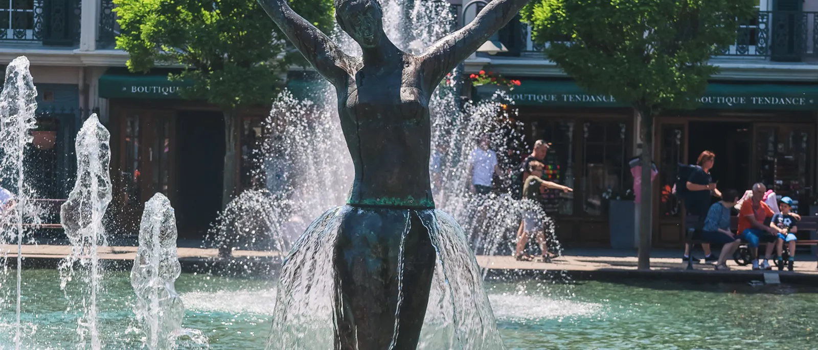 Fontaine ornée d’une danseuse en bronze devant une façade rose et des drapeaux français, à Europa-Park
