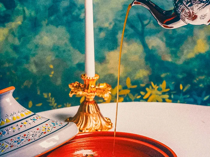 Plat en cocotte orange avec théière argentée versant un jus