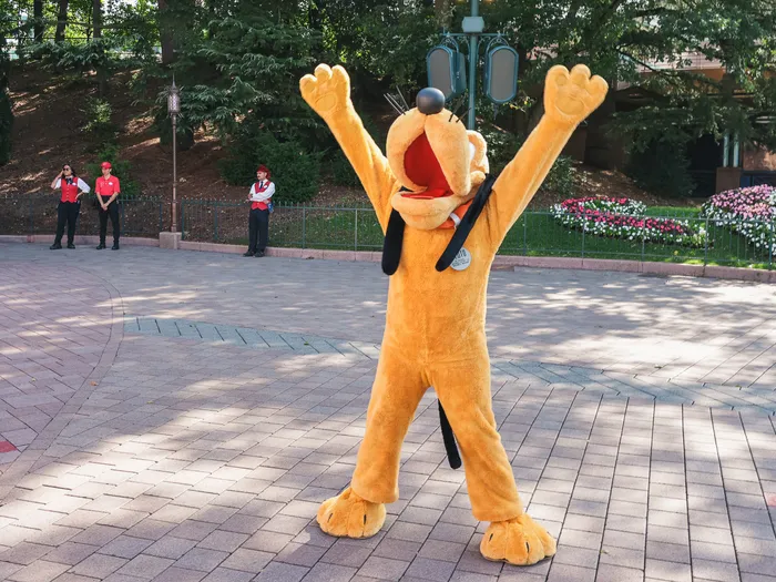 Pluto pattes levées sur le parcours de la parade Disney Stars on Parade, cast members en arrière-plan