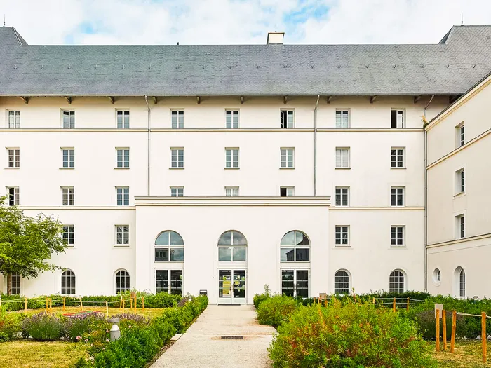 Façade blanche à toit d’ardoise du B&B Hôtel près de Disney devant un jardin traversé d’une allée