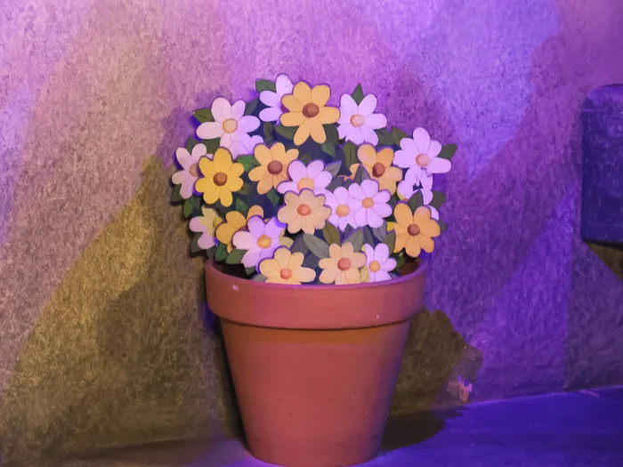 Pot en terre cuite garni de fleurs peintes en bois, éclairé en violet dans un décor de l’attraction Pinocchio