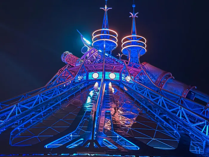 Dôme d’Hyperspace Mountain éclairé en bleu la nuit, ses deux tours turquoise et une affiche Star Wars en façade.