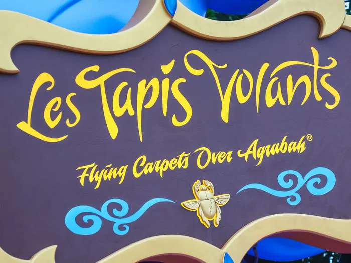 Enseigne dorée « Les Tapis Volants - Flying Carpets Over Agrabah » sur fond brun de l’attraction
