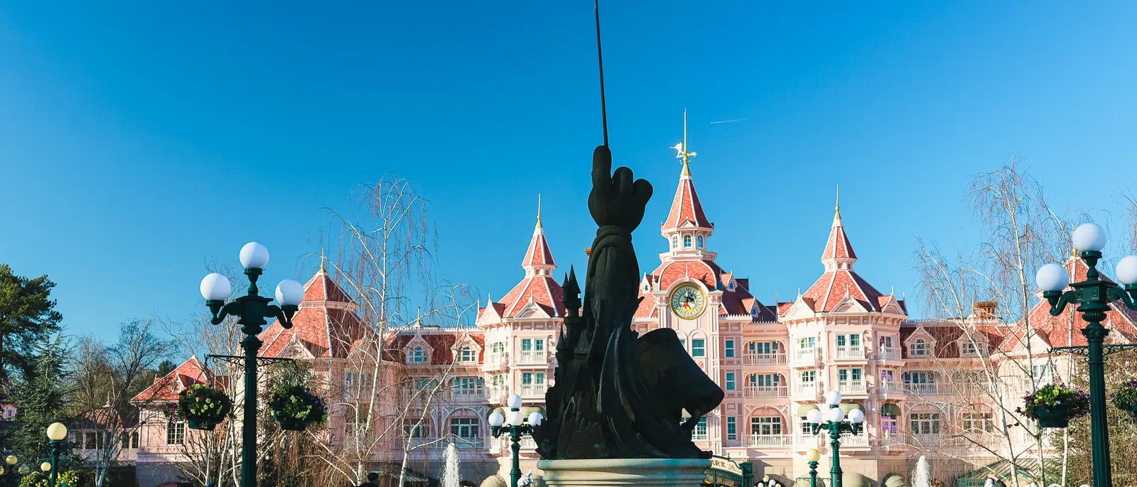 La façade rose du Disneyland Hotel et la statue de Mickey magicien pointant sa baguette vers le ciel bleu.