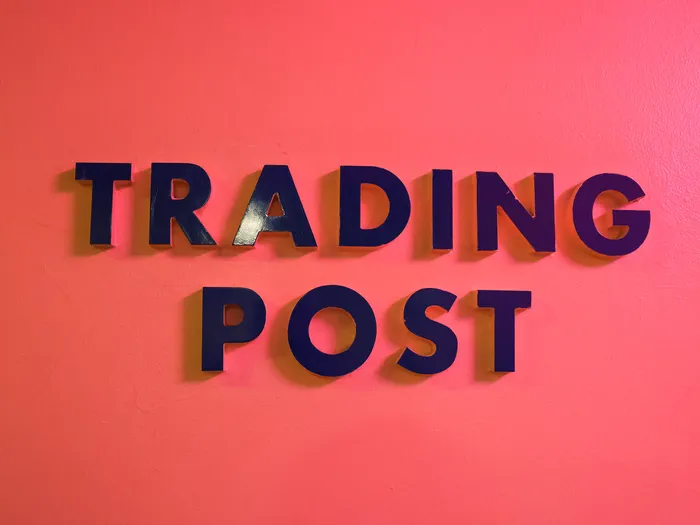 Navy blue "TRADING POST" letters fixed to a bright pink wall in the shop