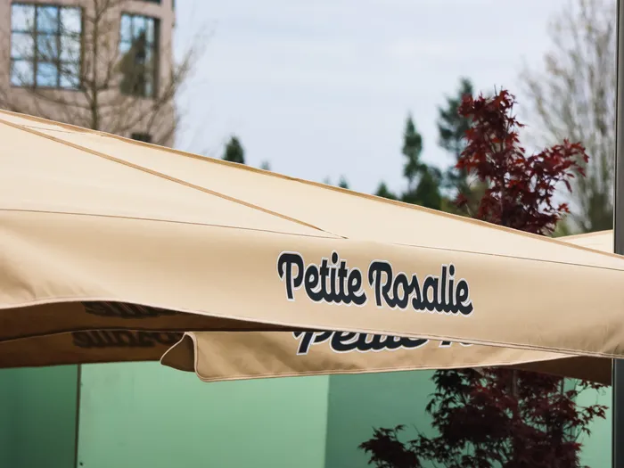 Parasol beige portant l’inscription Petite Rosalie devant un arbre au feuillage rouge