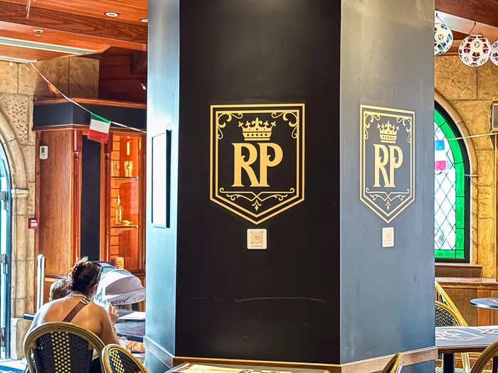 Salle du pub avec pilier noir au logo doré RP et chaises bistrot
