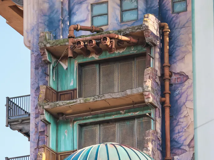 Détail de la façade vieillie du Tower of Terror avec tuyaux rouillés, balcons craquelés et enduit écaillé bleuté.