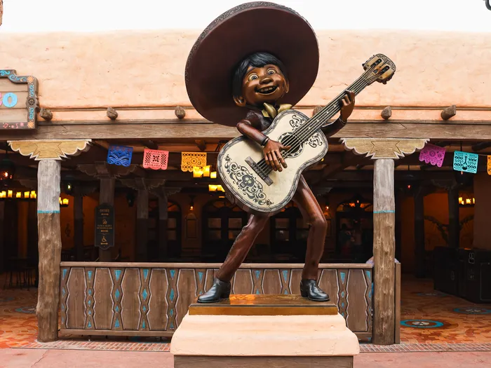 Statue de Miguel en pied avec sa guitare devant l'entrée à guirlandes de papel picado de Casa de Coco