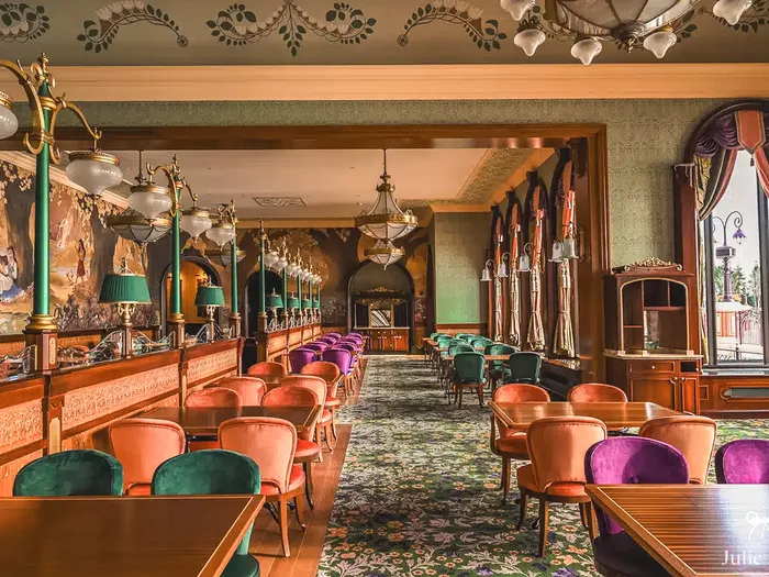 Salle verte ornée de fresques, lampes art nouveau et fauteuils de velours du restaurant The Regal View à Disneyland Paris
