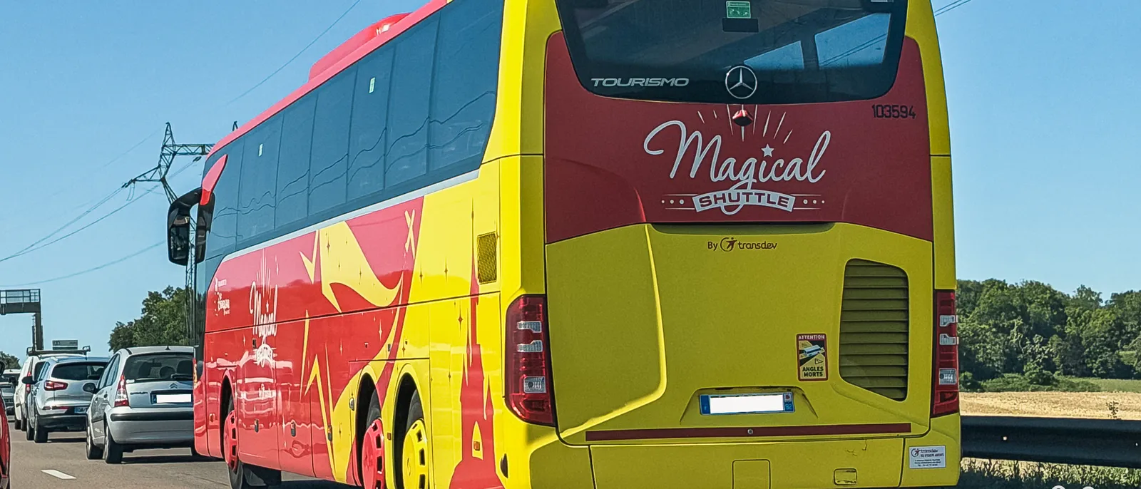 Autocar jaune et rouge Magical Shuttle vu de l’arrière sur l’autoroute, navette aéroport de Disneyland Paris.