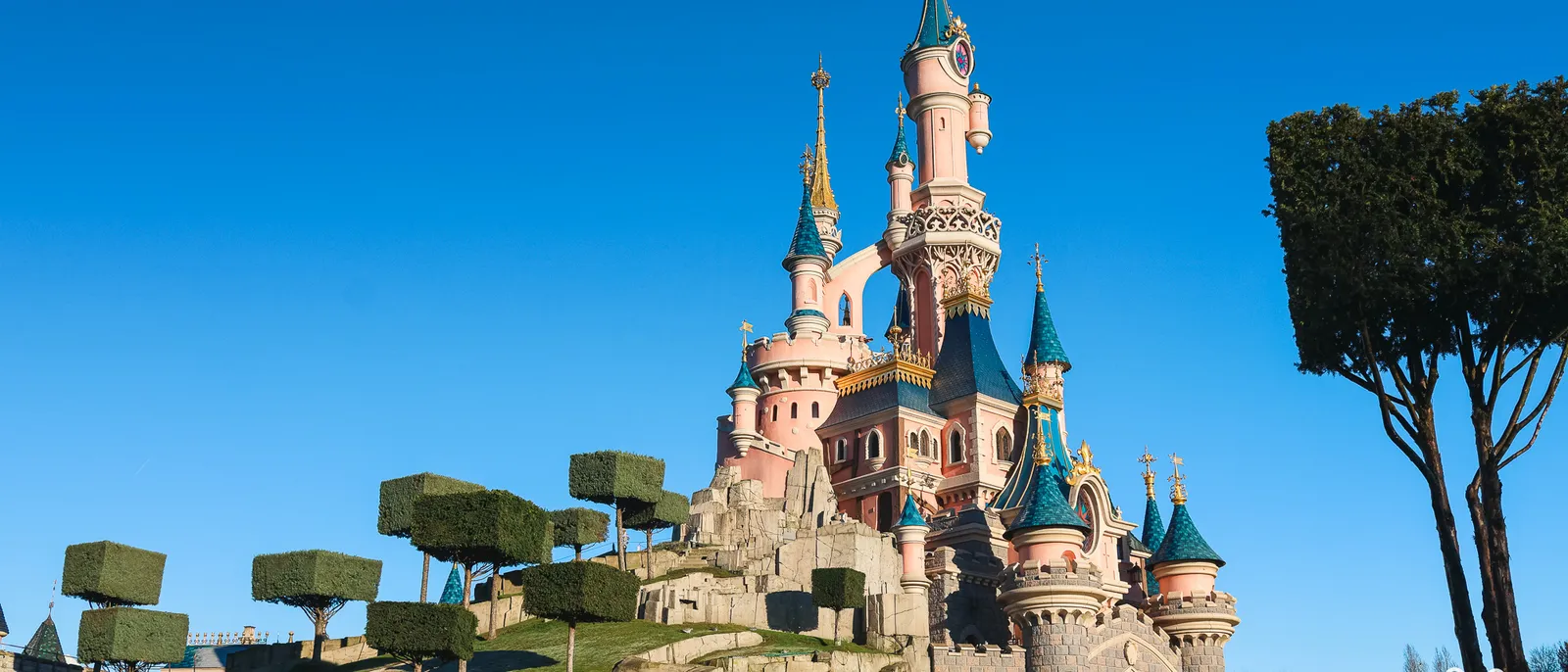 Le château de la Belle au Bois Dormant vu de côté depuis la butte aux arbres taillés, sous un ciel bleu vif