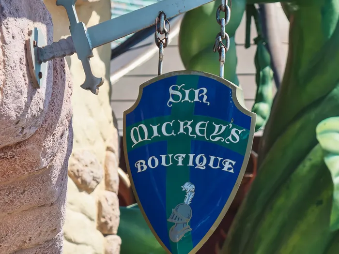 Crest-shaped sign of Sir Mickey’s Boutique hanging from a sword, near the giant green beanstalk