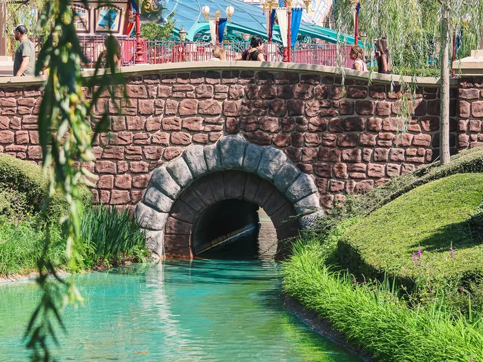 Le manège Dumbo the Flying Elephant aperçu au-dessus d’un pont de pierre et d’un canal turquoise à Fantasyland