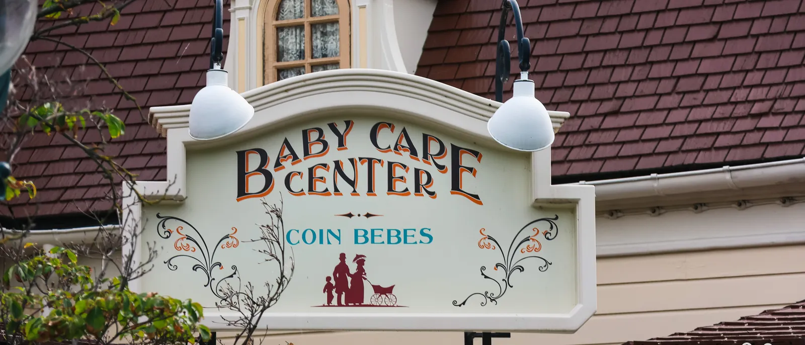 Enseigne peinte « Baby Care Center Coin Bébés » avec silhouette d’une famille, sous deux lampes, Disneyland Paris.