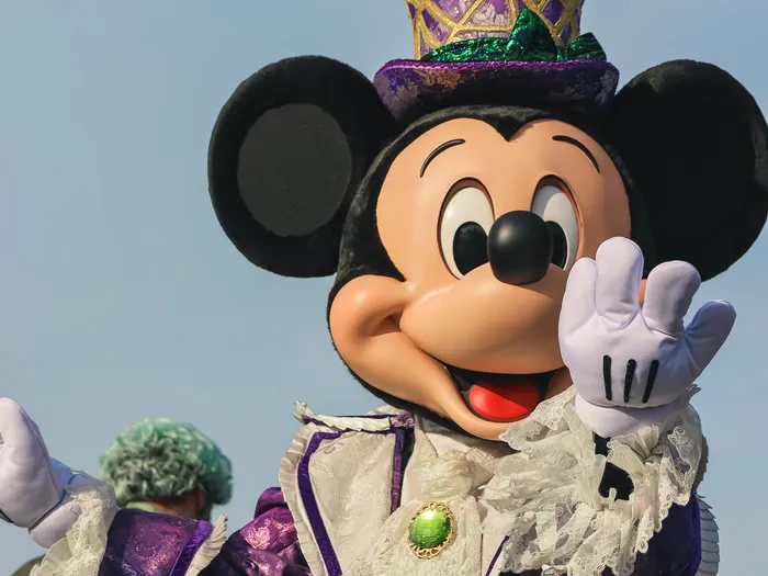 Gros plan de Mickey saluant, vêtu d’un costume violet et d’un haut-de-forme pailleté, lors de la célébration Halloween du Parc Disneyland.