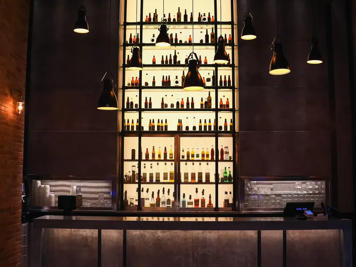 Bar du Bleecker Street Lounge à l’Hotel New York, haut mur de bouteilles rétroéclairé et suspensions industrielles